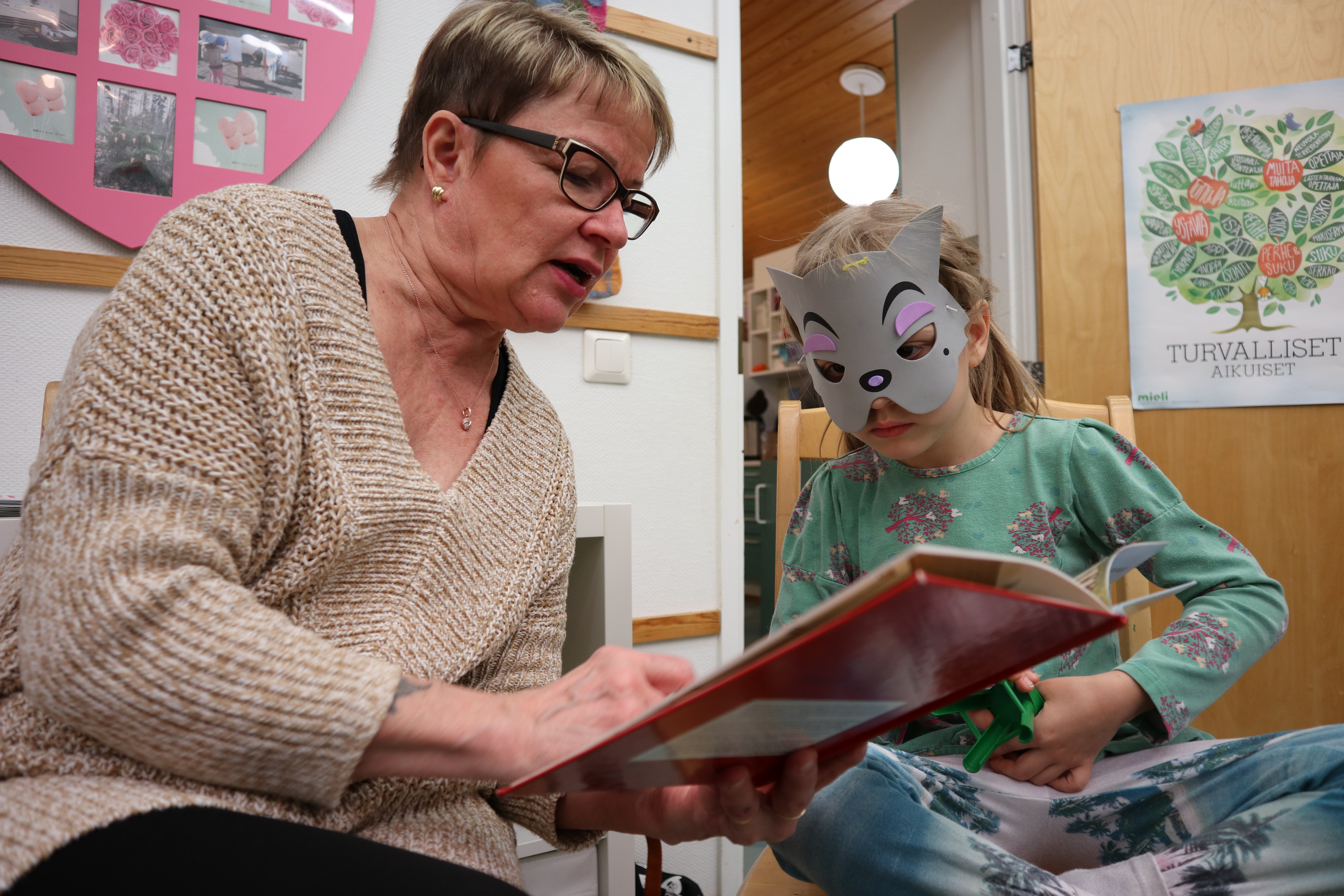 Vapaaehtoinen varamummu lukee kirjaa koiranaamio kasvoilla olevalle noin 5-vuotiaalle lapselle.